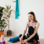 a woman tying her shoelaces on a yoga mat