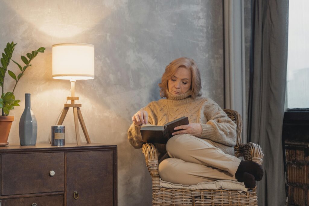 A person relaxing with a book in a cozy chair under soft lighting, taking time for self-care.